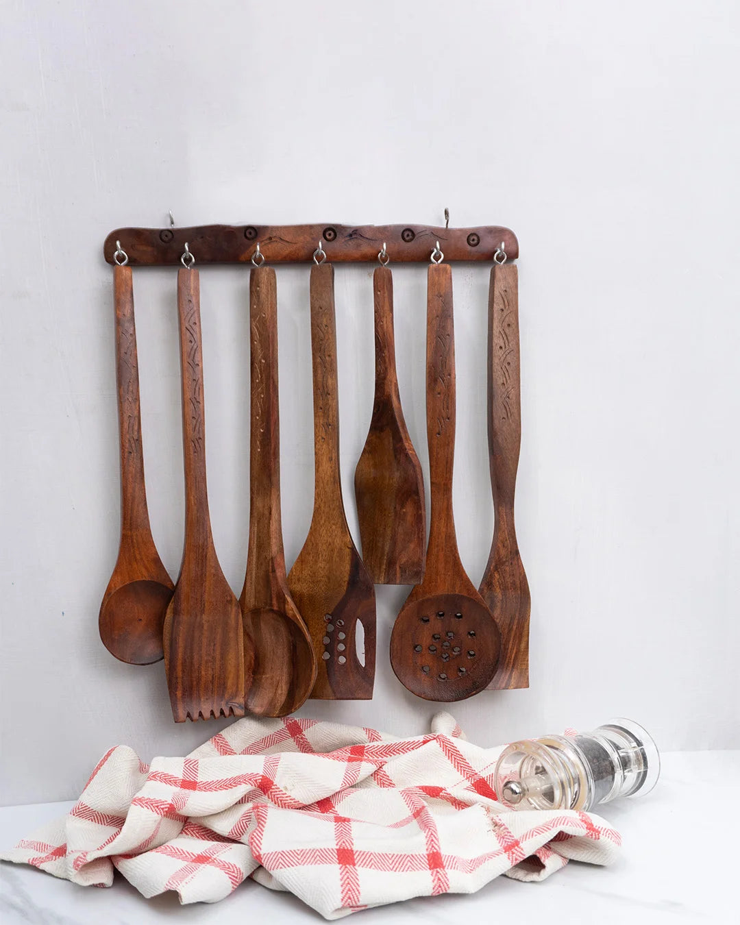 Set of wooden spoons hanging on a rack with a kitchen towel and salt and pepper shakers below.