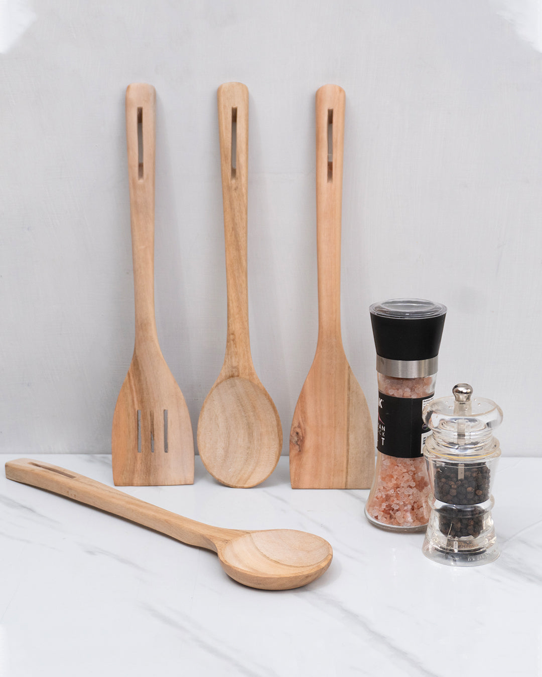 Set of wooden utensils including spoons and a spatula on a white surface with salt and pepper shakers.