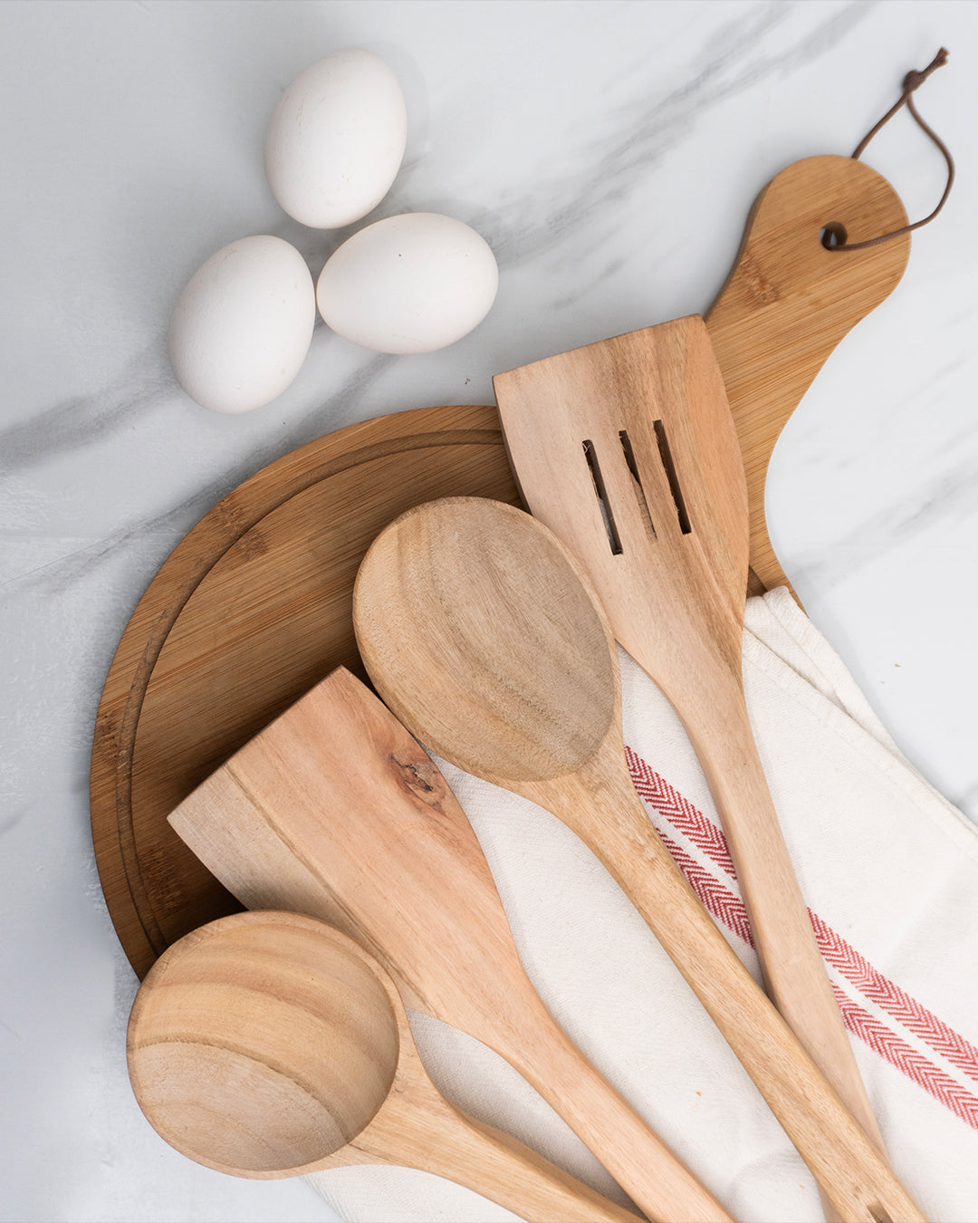Wooden kitchen utensils including spoons and a spatula on a marble surface with eggs.